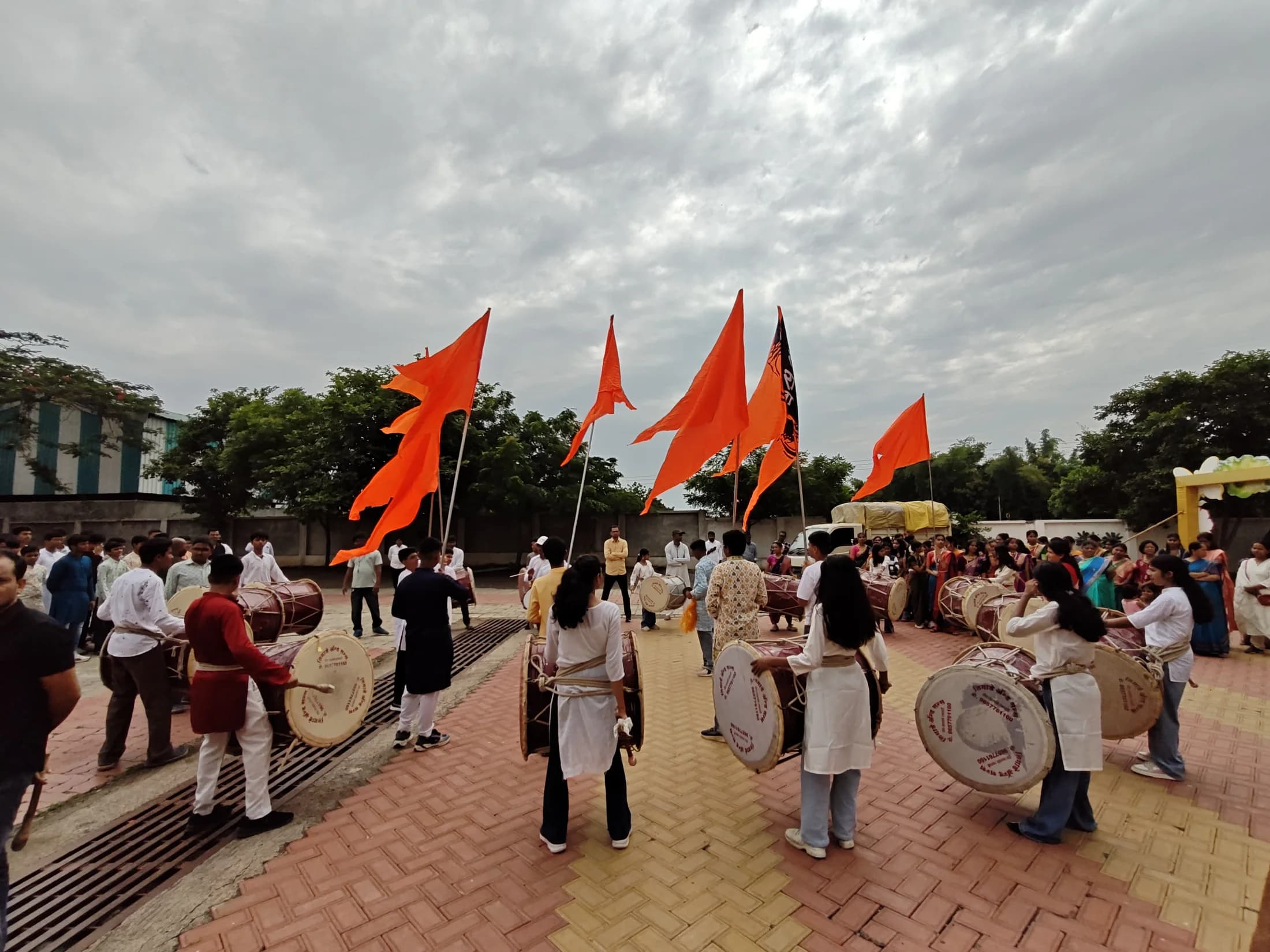 Students playing dhol with saffron flags during Ganesha Week