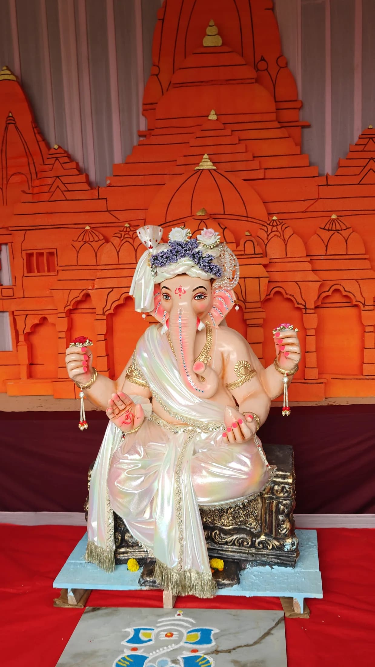 Lord Ganesha idol placed against an ornate orange temple backdrop